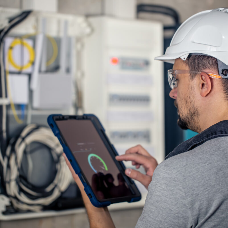 Man, an electrical technician working in a switchboard with fuses, uses a tablet. Man, an electrical technician working in a switchboard with fuses. Installation and connection of electrical equipment.
